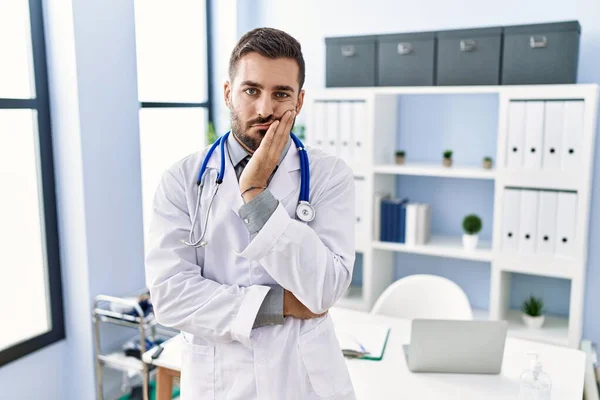 在诊所里穿着医生制服和听诊器的英俊的惊慌失措的男人看上去疲惫不堪 对交叉双臂的抑郁症感到厌烦 — 图库照片