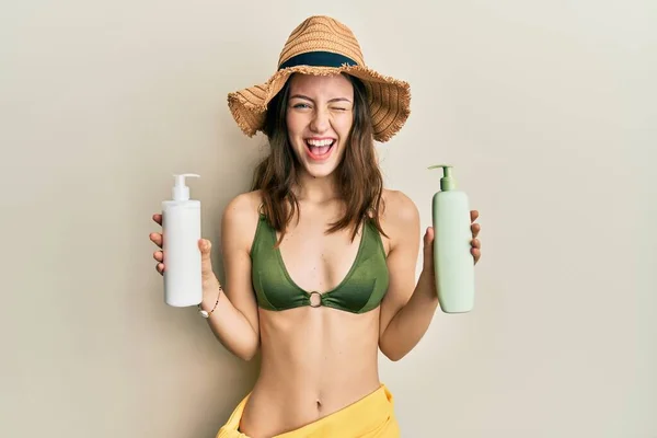 Young Brunette Woman Wearing Bikini Holding Sunscreen Lotions Winking Looking — Stockfoto