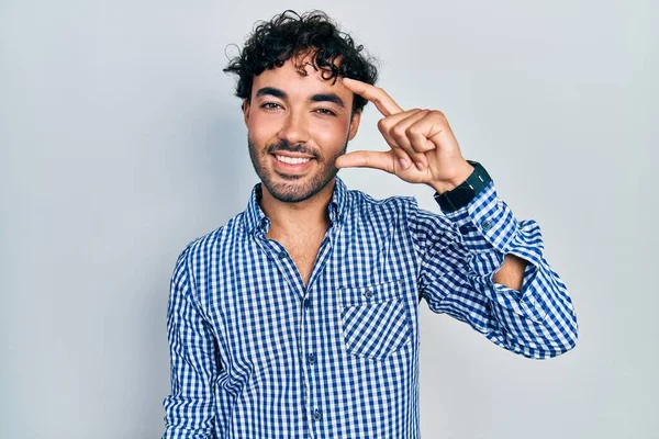 カジュアルな服を着た若いヒスパニック系の男が笑顔で 指を見てカメラで小さなサイズの看板をして手で自信を持ってジェスチャー 概念を測定し — ストック写真