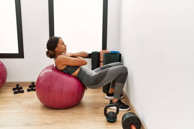 Spor merkezinde formda top kullanarak karın kaslarını çalıştıran genç Latin kadın.