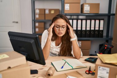 Küçük işletme şirketinde çalışan Latin kökenli genç bir kadın. Elleri başının üstünde, stres yüzünden baş ağrısı çekiyor. migren ağrısı. 