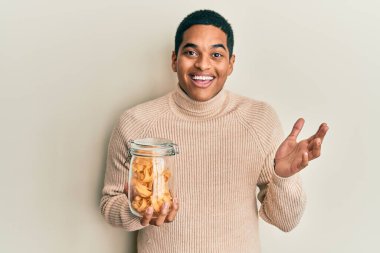 Genç, yakışıklı İspanyol adam elinde makarna dolu kavanozla başarıyı kutluyor mutlu bir gülümsemeyle ve kazanan yüz ifadesini kaldırarak. 