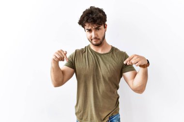 İzole edilmiş beyaz arka planda dikilen İspanyol adam üzgün ve üzgün görünüyor, parmaklarıyla yönü gösteriyor, mutsuz ve depresif.. 