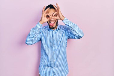 Sakallı, sıradan mavi tişörtlü İspanyol bir adam dürbün gibi hareket ediyor. Dilini çıkarıyor, gözleri parmaklarından bakıyor. çılgın ifade. 