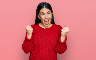 Güzel esmer kadın gündelik kazak giyip gururla bağırıyor zaferi ve başarıyı kutluyor. Kollarını kaldırıp heyecanla bekliyor. 