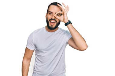 Sakallı, günlük beyaz tişörtlü genç adam el hareketleriyle gülümsüyor ve mutlu yüzüyle parmaklarının arasından bakıyor.. 