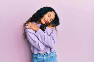 Gündelik kıyafetler giyen, mutlu ve olumlu bir şekilde kendine sarılan, kendinden emin gülümseyen genç Latin bir kadın. Sevgi ve özgüven. 