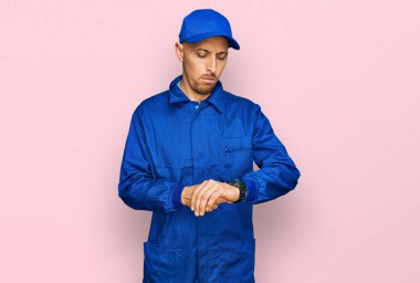 Kel, sakallı, işçi tulumu giyen, kol saati takan, rahat ve kendinden emin bir adam. 