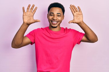 Casua tişörtü giyen genç Afro-Amerikalı adam on numarayı gösterip gösterirken kendinden emin ve mutlu gülümsüyor.. 