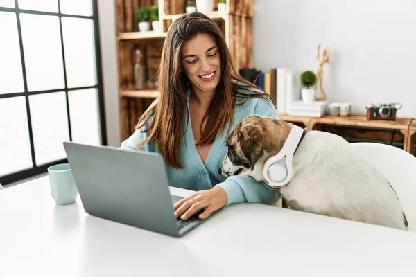 家でヘッドフォンを身に着けている犬とテーブルの上に座ってラップトップを使用して若い女性 — ストック写真