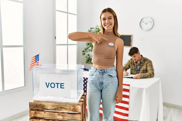 Young american voter woman smiling happy pointing with finger to baddge at electoral college.