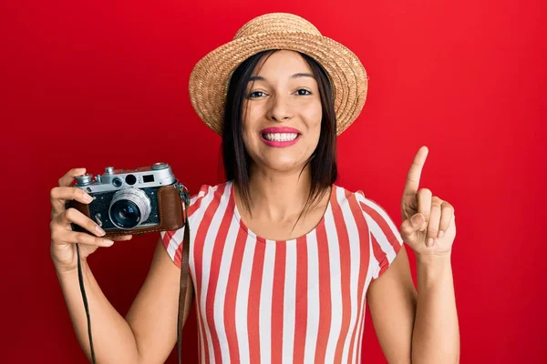 Yazlık şapkalı genç Latin kadın elinde antika bir kamerayla gülümsüyor ya da bir soru işareti yapıyor mutlu bir yüzle, bir numara 