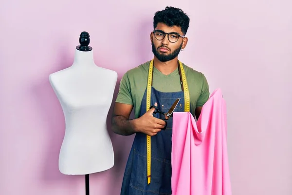 髭を生やしたドレスメーカーのデザイナーがハサミと布を持っているアラブ人男性は混乱した表情 疑わしい概念 — ストック写真