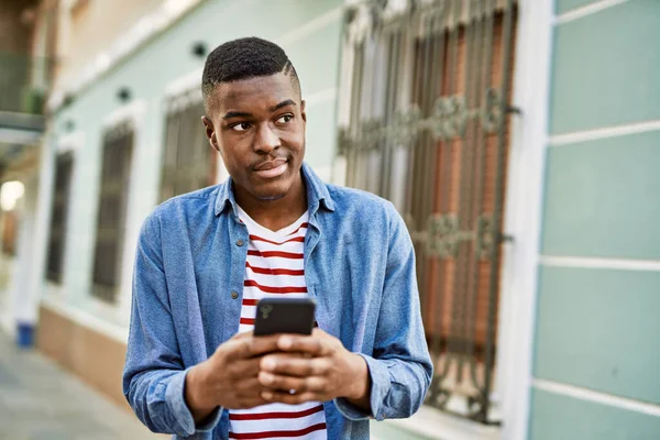Genç Afrikalı Amerikalı adam şehirde akıllı telefon kullanarak mutlu bir şekilde gülümsüyor..