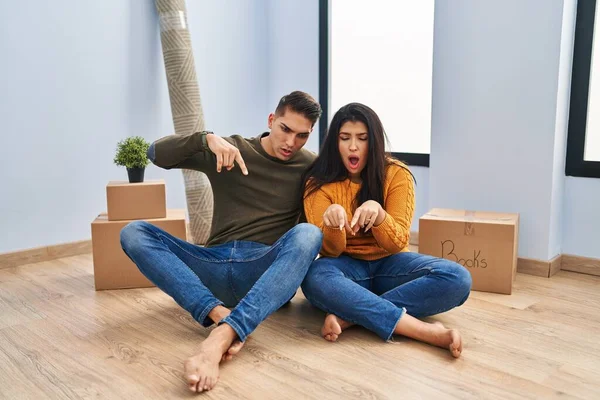 Young Couple Sitting Floor New Home Pointing Fingers Showing Advertisement — 스톡 사진