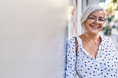 Orta yaşlı bir kadın sokakta kendine güvenerek gülümsüyor.