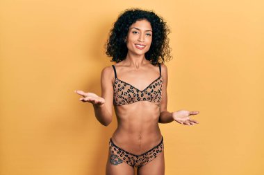 Genç Latin kız bikini giyiyor, neşeli gülümsüyor ve kollarını açıyor. Hoş geldin, olumlu ve kendinden emin selamlar. 