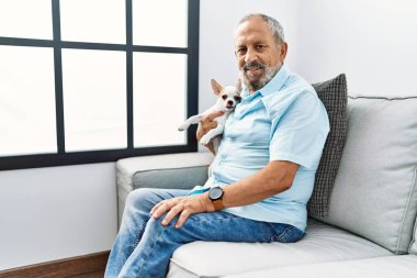 Yaşlı, gri saçlı, gülümseyen ve elinde Chihuahua tutan adam.