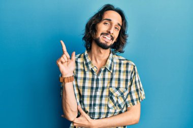 Yüzünde kocaman bir gülümseme olan, gündelik kıyafetler giyen genç İspanyol adam, kameraya el ve parmak ile bakıyor.. 