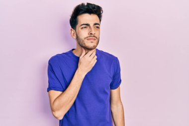 Gündelik tişört giyen genç İspanyol adam ağrılı boynuna dokunuyor, boğazı ağrıyor grip, mantar ve enfeksiyon kapmış. 