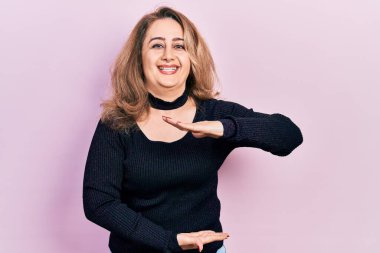 Orta yaşlı beyaz kadın, sıradan kıyafetler giyiyor. Elleriyle büyük ve büyük boy işareti gösteriyor. Ölçü sembolü. Kameraya bakıp gülümsüyor. ölçüm kavramı. 