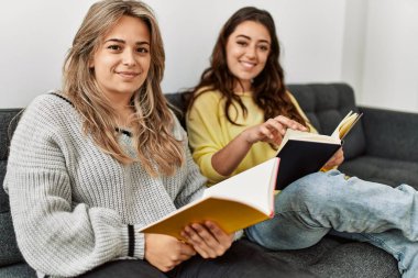 Evdeki kanepede kitap okuyan genç bir çift..