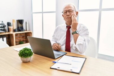 Ofiste çalışan kıdemli bir adam diş ağrısı ya da diş ağrısı yüzünden bilgisayarla ağza dokunuyor. dişçi 