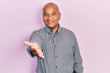 Orta yaşlı, sıradan kıyafetler giyen, dostça gülümseyen, selamlaşmak ve selamlamak için el sıkışan bir Latin. başarılı iş. 