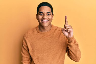 Genç, yakışıklı, günlük kışlık süveter giyen, kendine güvenen ve mutlu bir şekilde gülümseyen, bir numaralı parmağını gösteren İspanyol.. 