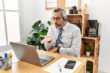 Orta yaşlı İspanyol iş adamı ofiste çalışıyor operatör kulaklığı takıyor kameraya bakıyor ve havada el ele öpüşerek sevimli ve seksi oluyor. aşk ifadesi. 