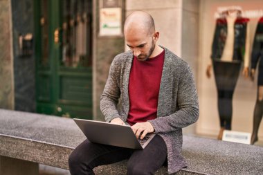 Genç adam dizüstü bilgisayar kullanıyor. Sokakta bankta oturuyor.