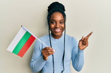 Saçları örülmüş, elinde Bulgar bayrağı olan Afro-Amerikalı bir kadın gülümsüyor. 