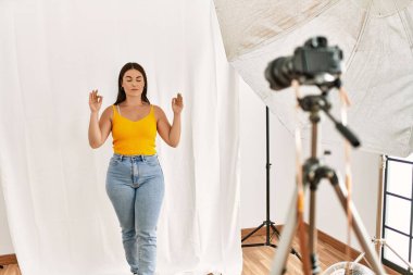 Fotoğrafçılık stüdyosunda model gibi davranan genç ve güzel İspanyol kadın rahatla ve gülümse gözleri kapalı parmaklarıyla meditasyon hareketi yapıyor. yoga konsepti. 