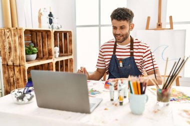 Sanat stüdyosunda dizüstü bilgisayar kullanan genç bir Arap sanatçı..