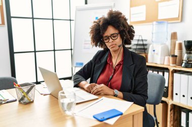 Ofiste çalışan afro saçlı Afrikalı bir kadın operatör kulaklığı takıyor. Uykulu ve yorgun görünüyor. Yorgunluktan ve akşamdan kalmalıktan yorgun.. 