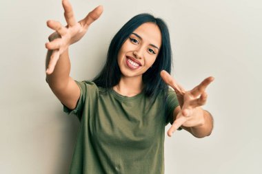 Gündelik tişört giyen genç İspanyol kız kameraya sarılmak için kollarını açmış gülümsüyor. Mutluluğu kucaklayan neşeli bir ifade.. 