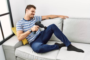 Evde perküsyon tabancası kullandığından emin bir şekilde gülümseyen İspanyol genç adam.