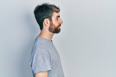 Sakallı, günlük gri tişörtlü, rahat profil pozu veren, kendine güveni olan beyaz bir adam.. 