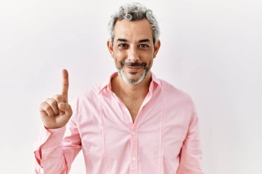 Orta yaşlı İspanyol bir adam izole edilmiş arka planda duruyor. Bir numarayı işaret ediyor ve gülümsüyor. Kendinden emin ve mutlu.. 