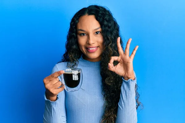 Genç Latin kadın elinde kahve tutuyor. Parmaklarıyla imza atıyor. Gülümsüyor. 