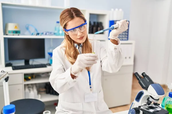 实验室里穿着科学家制服的金发年轻女士用吸盘倒液体 — 图库照片
