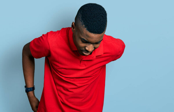 Young african american man wearing casual red t shirt suffering of backache, touching back with hand, muscular pain