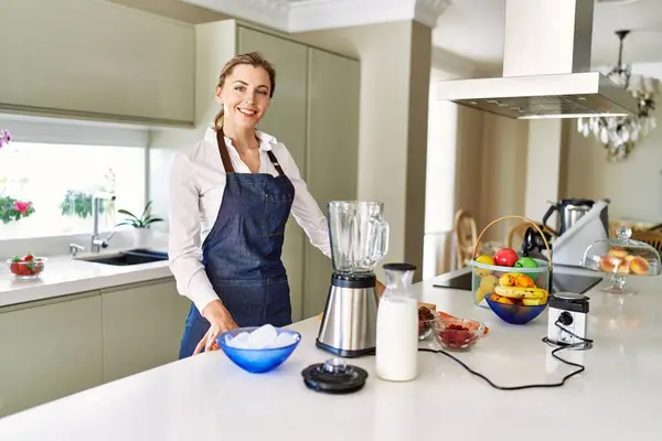 Genç sarışın kadın gülümsüyor. Mutfakta kendine güvenen smoothie pişiriyor.