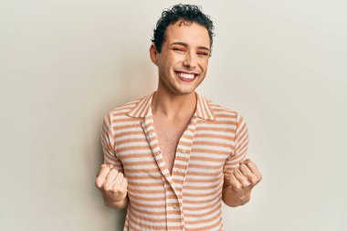 Makyaj yapan yakışıklı adam rahat tişört giyiyor. Çok mutlu ve heyecanlı. Kolları havada, gülümseyen ve başarı için bağıran kazanan jestler yapıyor. kutlama konsepti. 