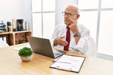 Ofiste çalışan kıdemli bir adam bilgisayarı kullanarak göze işaret ediyor jestini izliyor, şüpheli bir ifade. 