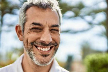 Orta yaşlı, kır saçlı, gülümseyen bir adam şehirde mutlu bir şekilde duruyor..