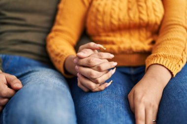 Man and woman couple sitting on sofa with hands together at home