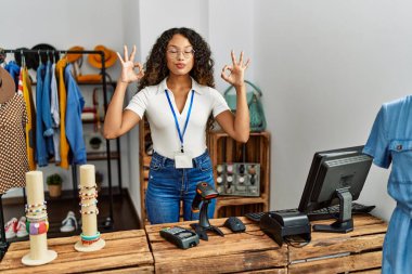Güzel İspanyol kadın giyim mağazasında çalışıyor rahatlıyor ve gözleri kapalı gülümsüyor parmaklarıyla meditasyon hareketi yapıyor. yoga konsepti. 