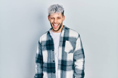 Modern boyalı saçlı, sıradan gömlekli genç İspanyol bir adam kameraya seksi bir ifadeyle bakıyor, neşeli ve mutlu bir yüzü var.. 