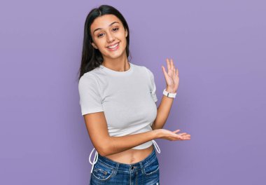 Günlük beyaz tişört giyen genç İspanyol kız gülümseyerek içeri girmeye davet ediyor. 